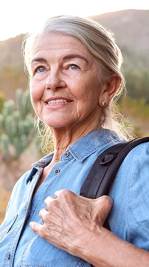 Woman in her 60s with silver hair smiling outdoors with a backpack